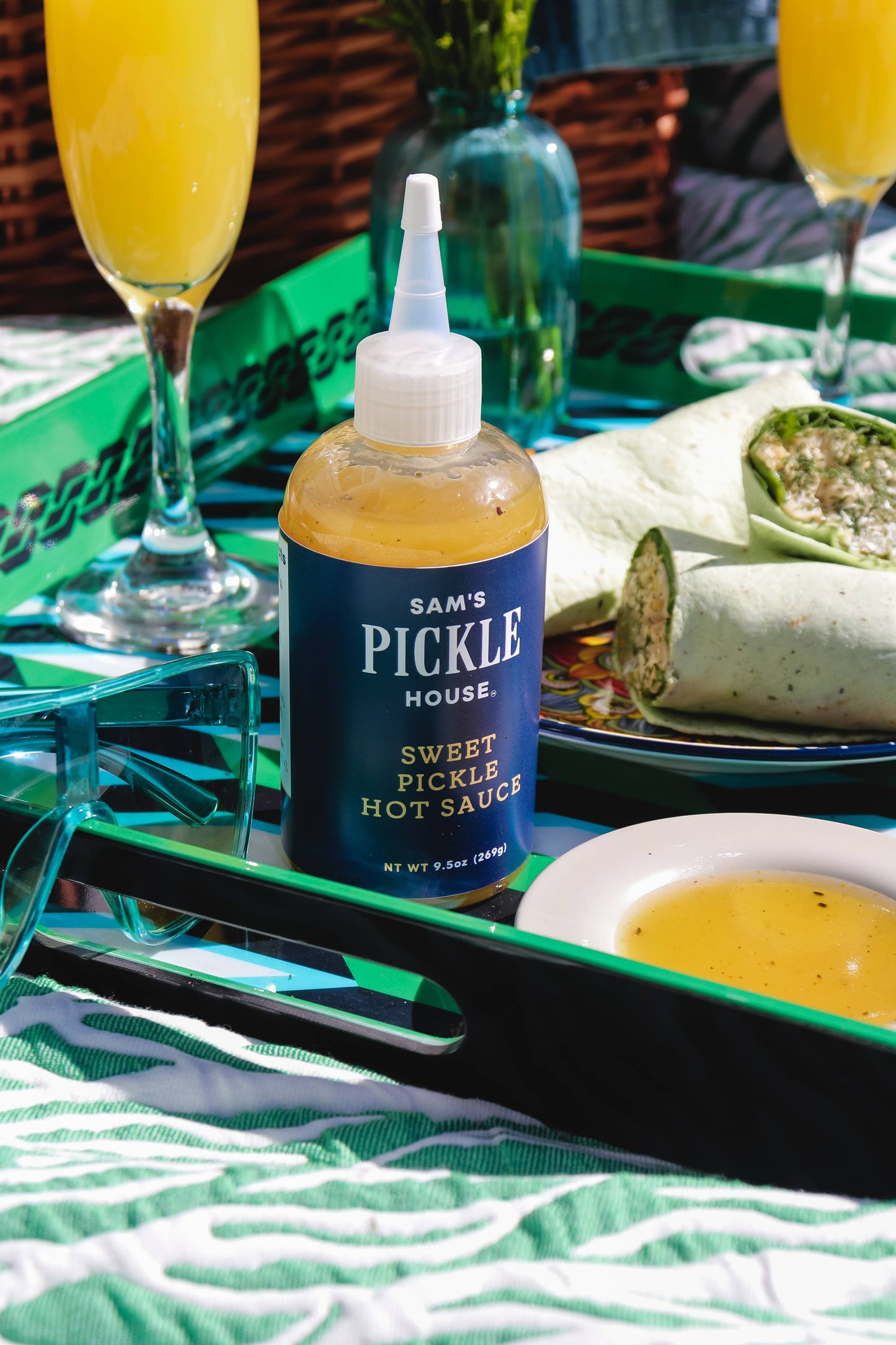 Bottle of Sam's Pickle House sweet pickle hot sauce on a tray with drinks and food.