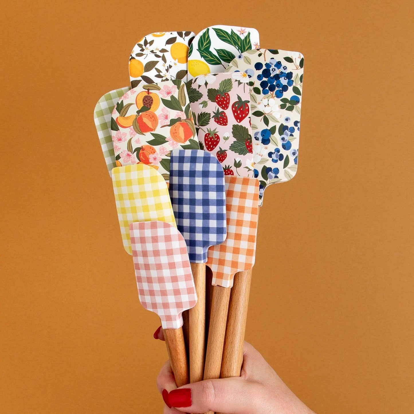 Set of colorful spatulas with patterned handles held against a brown background