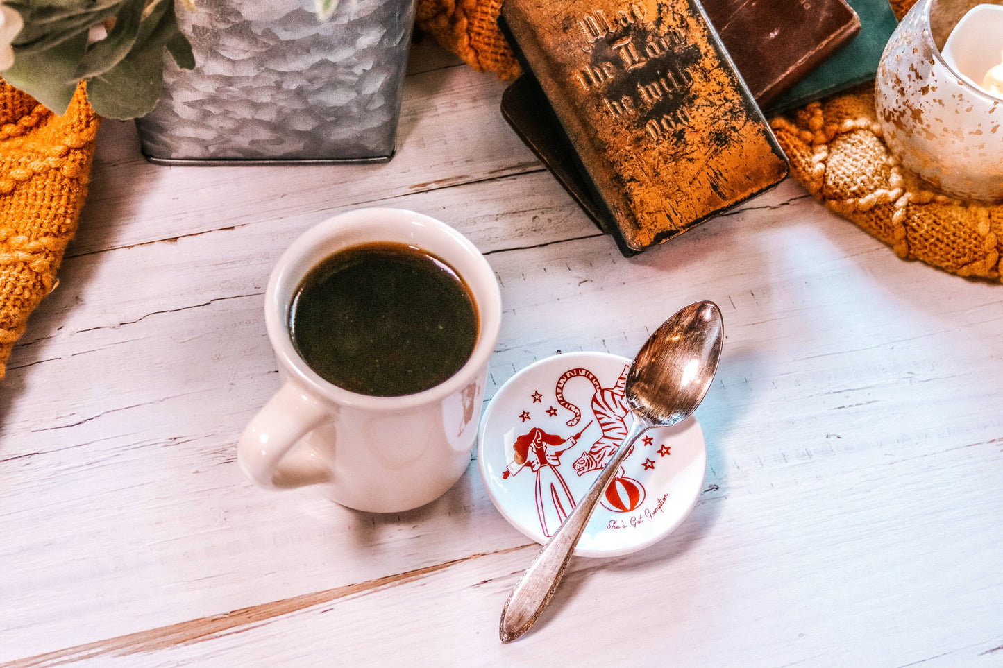 Cup of coffee with a spoon on a saucer, placed on a wooden surface with decorative items.
