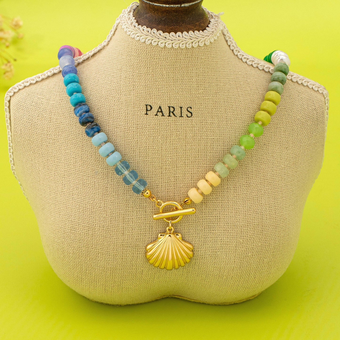 Colorful beaded necklace with a gold clasp on a mannequin bust labeled 'PARIS' against a yellow background