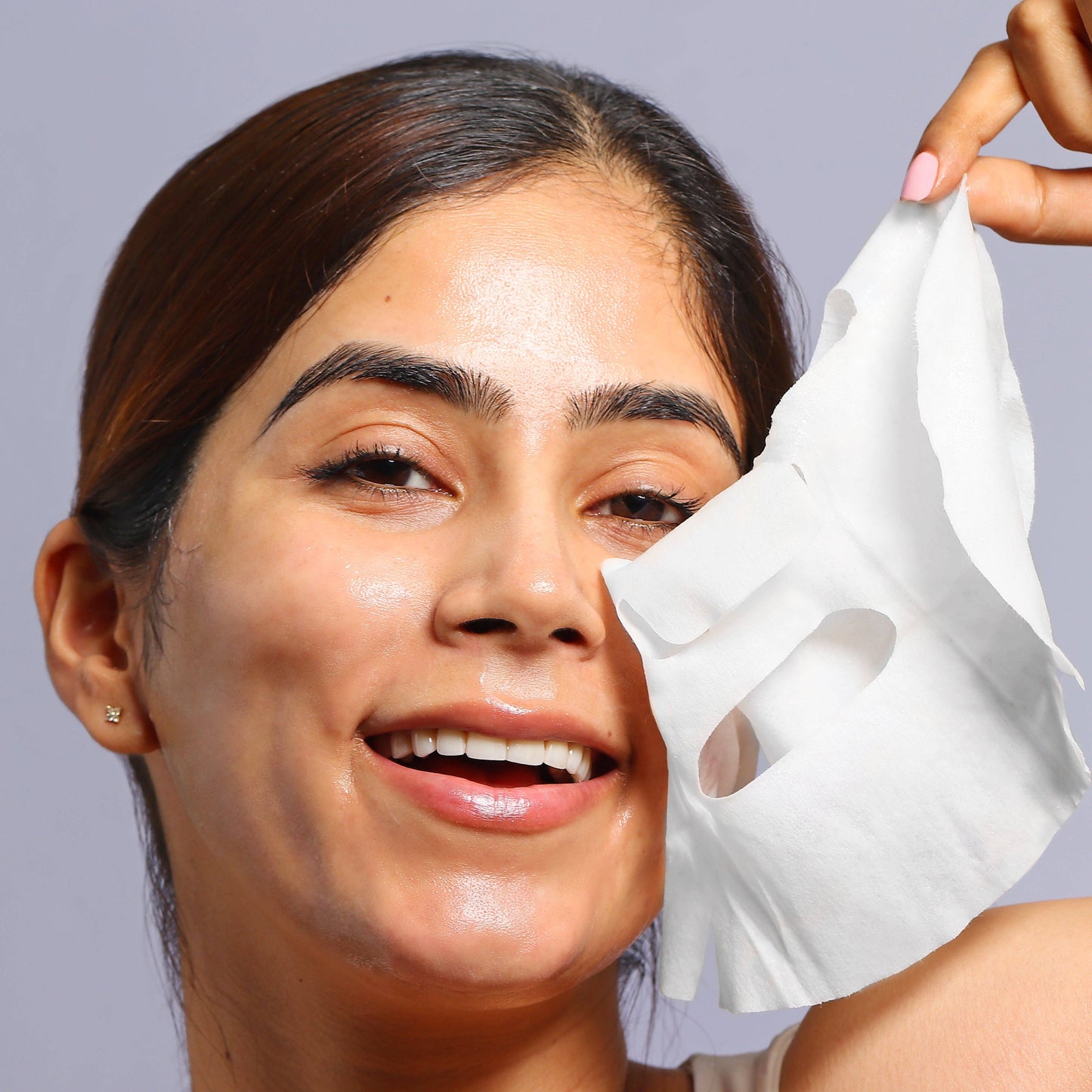 Woman applying a white sheet mask to her face against a gray background