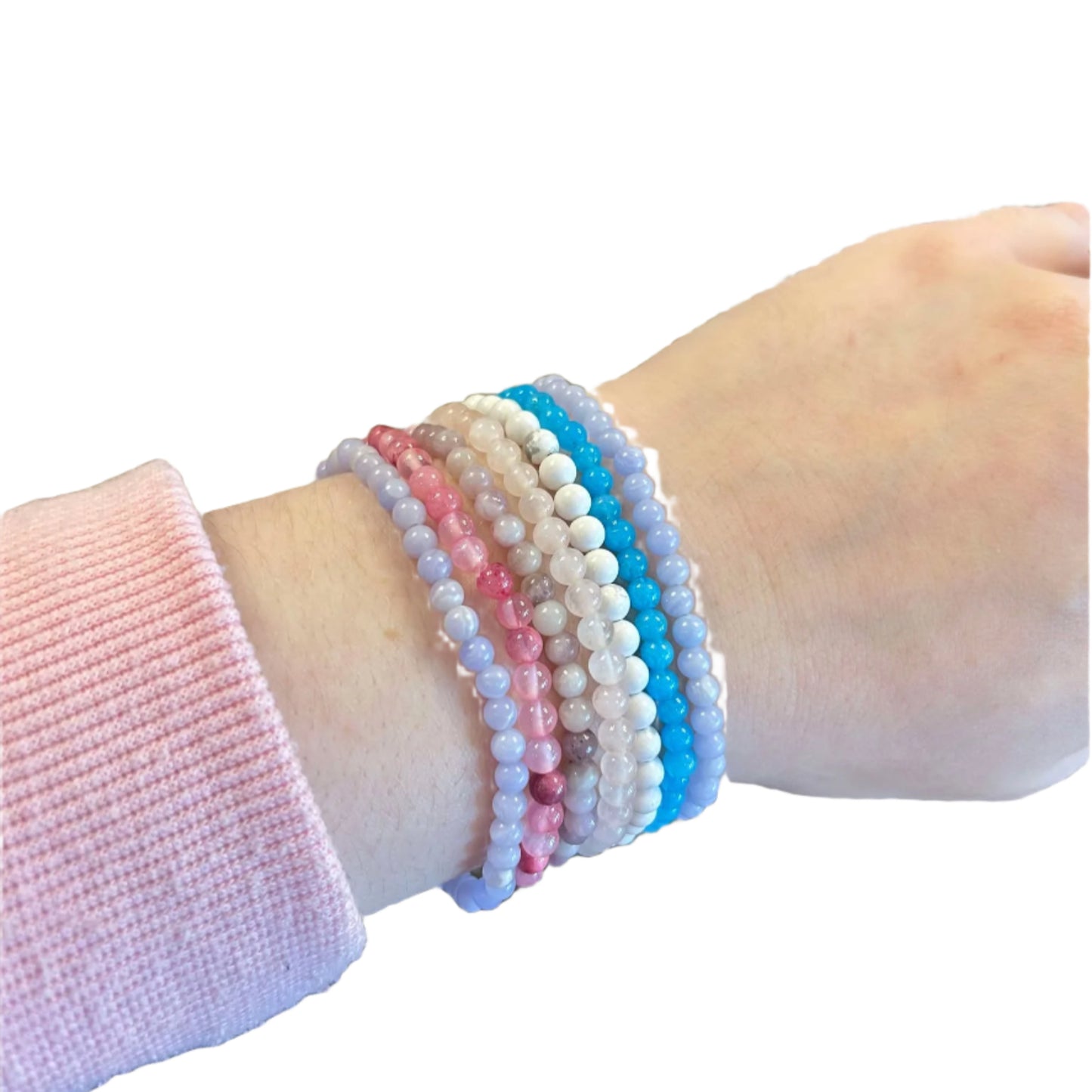 Several round gemstone beaded bracelets on a persons wrist, displayed on a white background