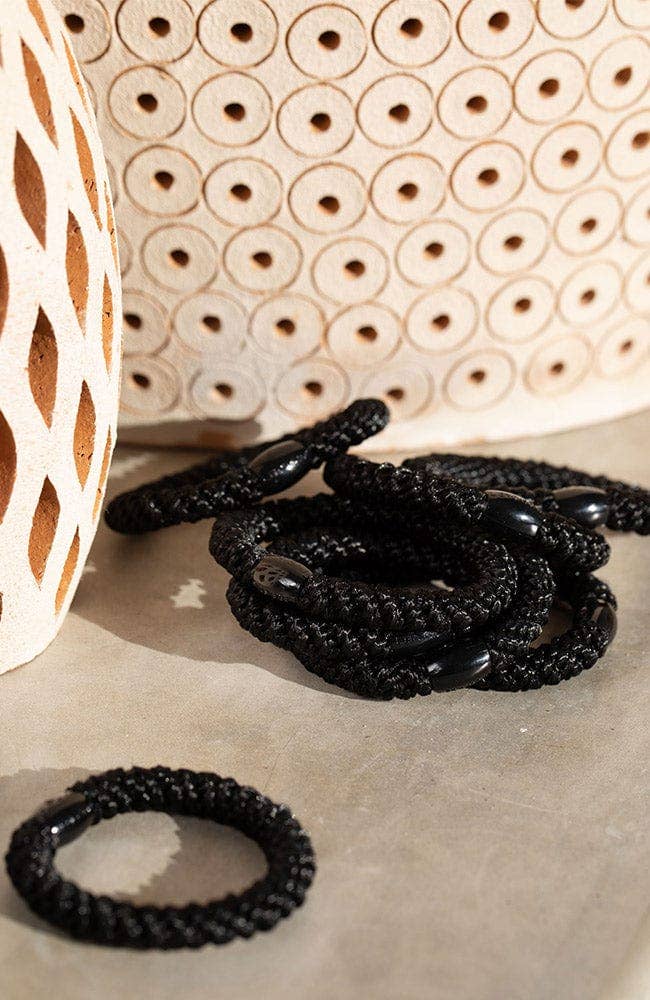 Black hair ties on a textured surface with a woven basket in the background