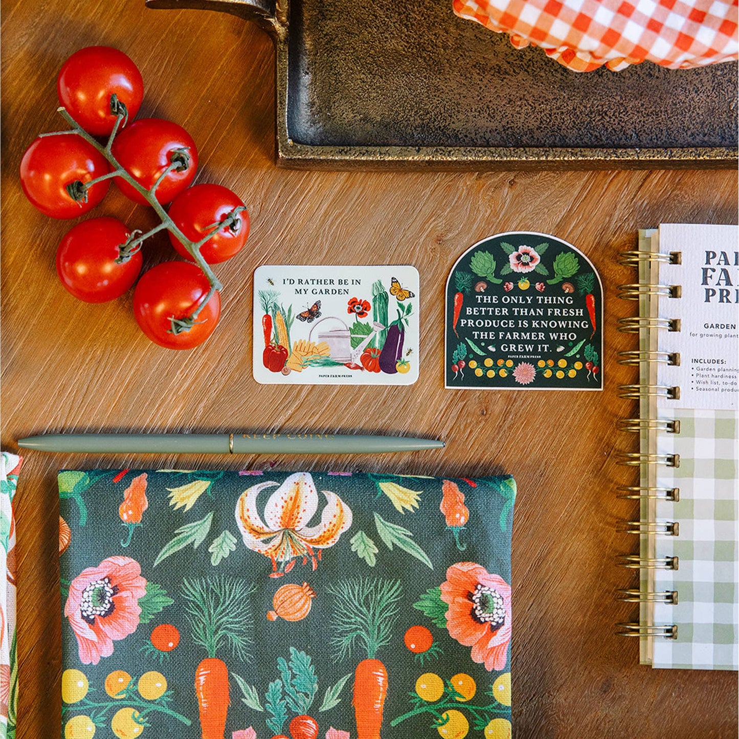 Wooden surface with tomatoes, a notebook, and decorative cards featuring garden-themed designs.