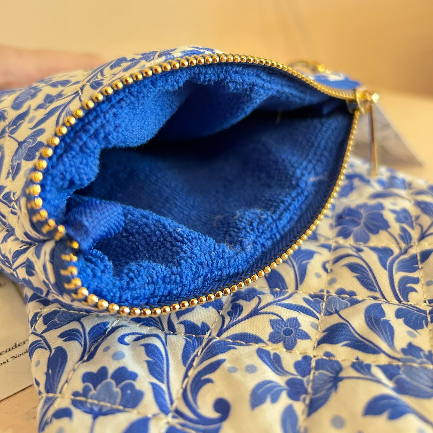Blue floral-patterned pouch with a gold zipper on a beige background