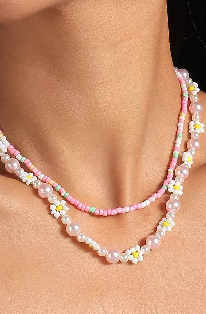 Two pearl necklaces with floral beads on a person's neck against a black background
