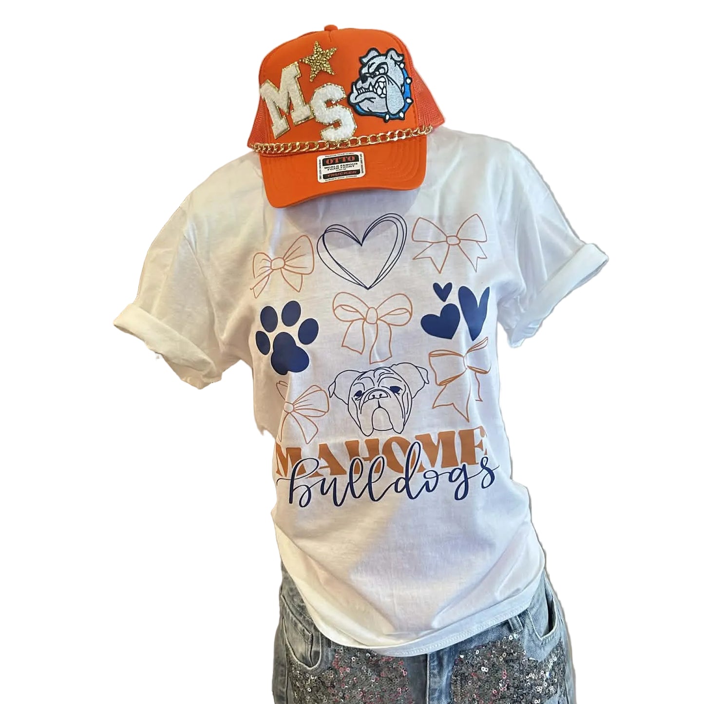 White t-shirt with bows, hearts, paw prints and a bulldog graphic with Mahomet Bulldogs text paired with an orange MS Bulldog hat on a mannequin against a white wall.