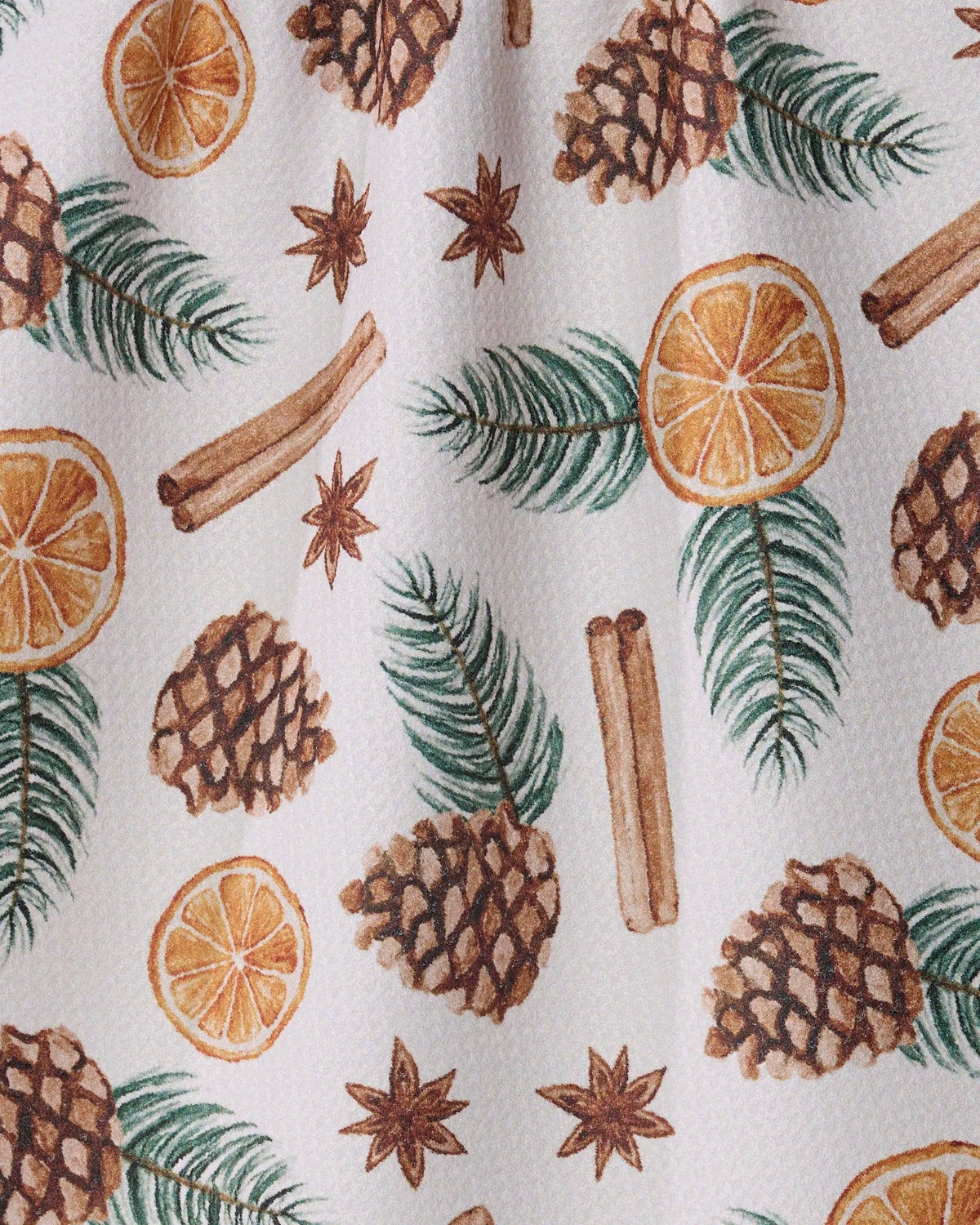 A close-up of a white fabric with a repeating Christmas-themed pattern featuring pinecones, cinnamon sticks, star anise, green pine needles, and dried orange slices.