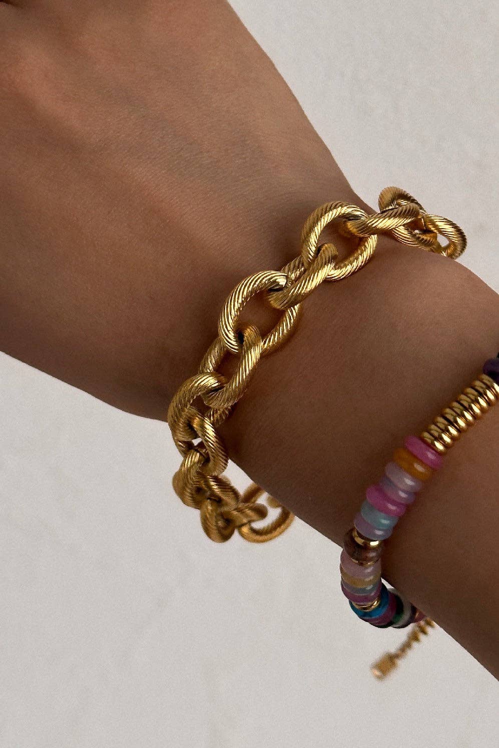 Gold chain bracelet on a wrist with a plain background