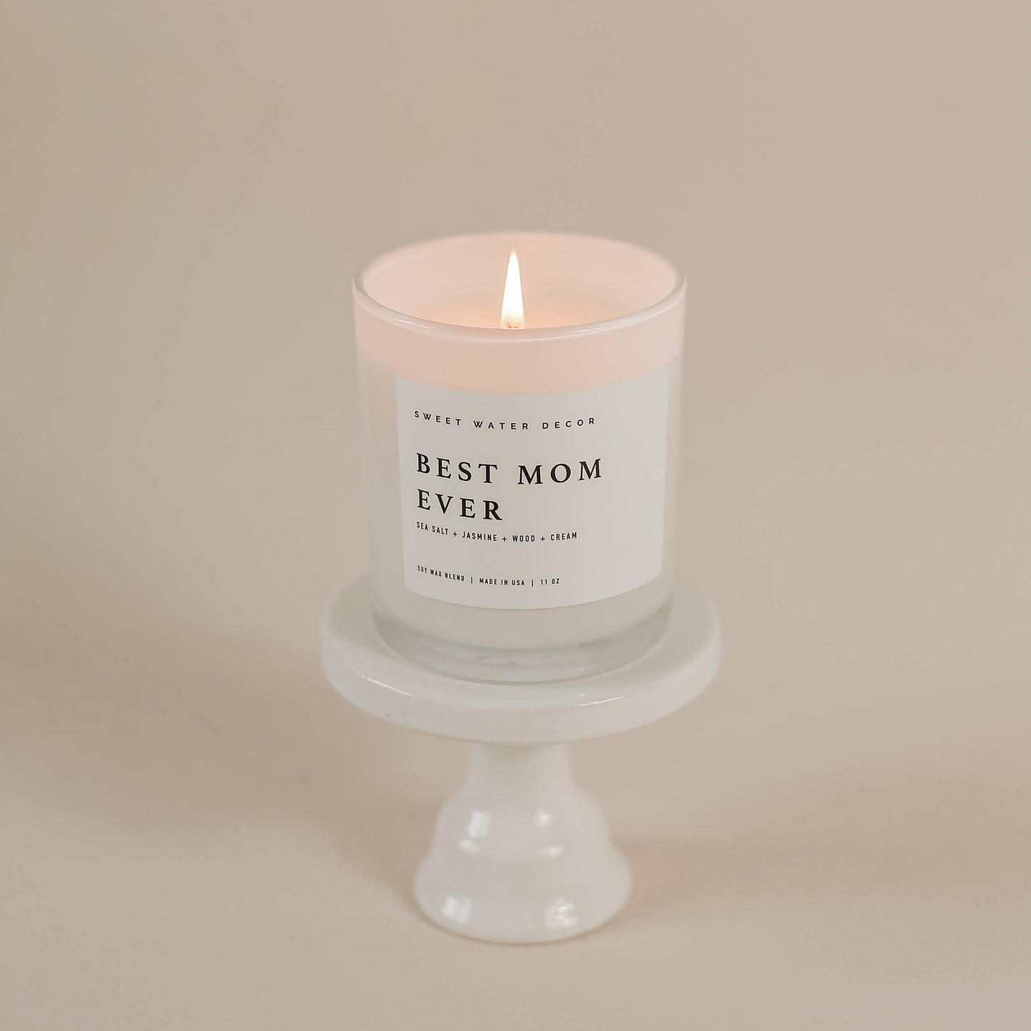 Candle with 'Best Mom Ever' label on a white pedestal against a beige background