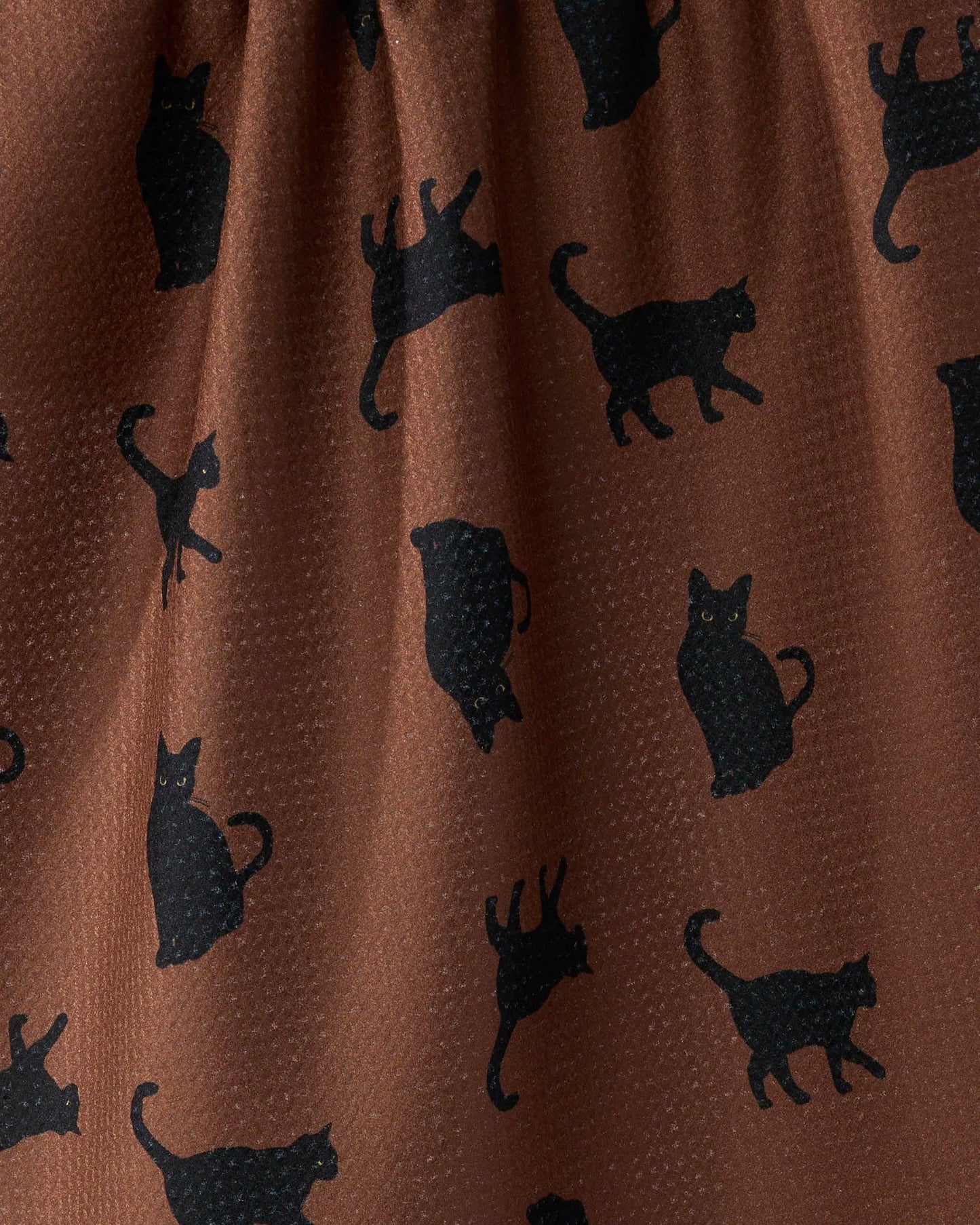 A close-up of a brown fabric with a repeating pattern of black cat silhouettes.