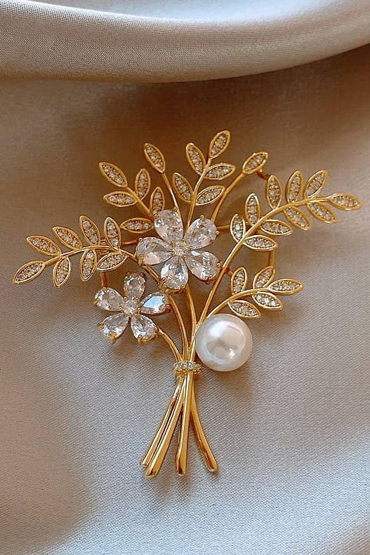 Gold flower bouquet shaped brooch with two rhinestone flowers and one pearl, on a cream silk background