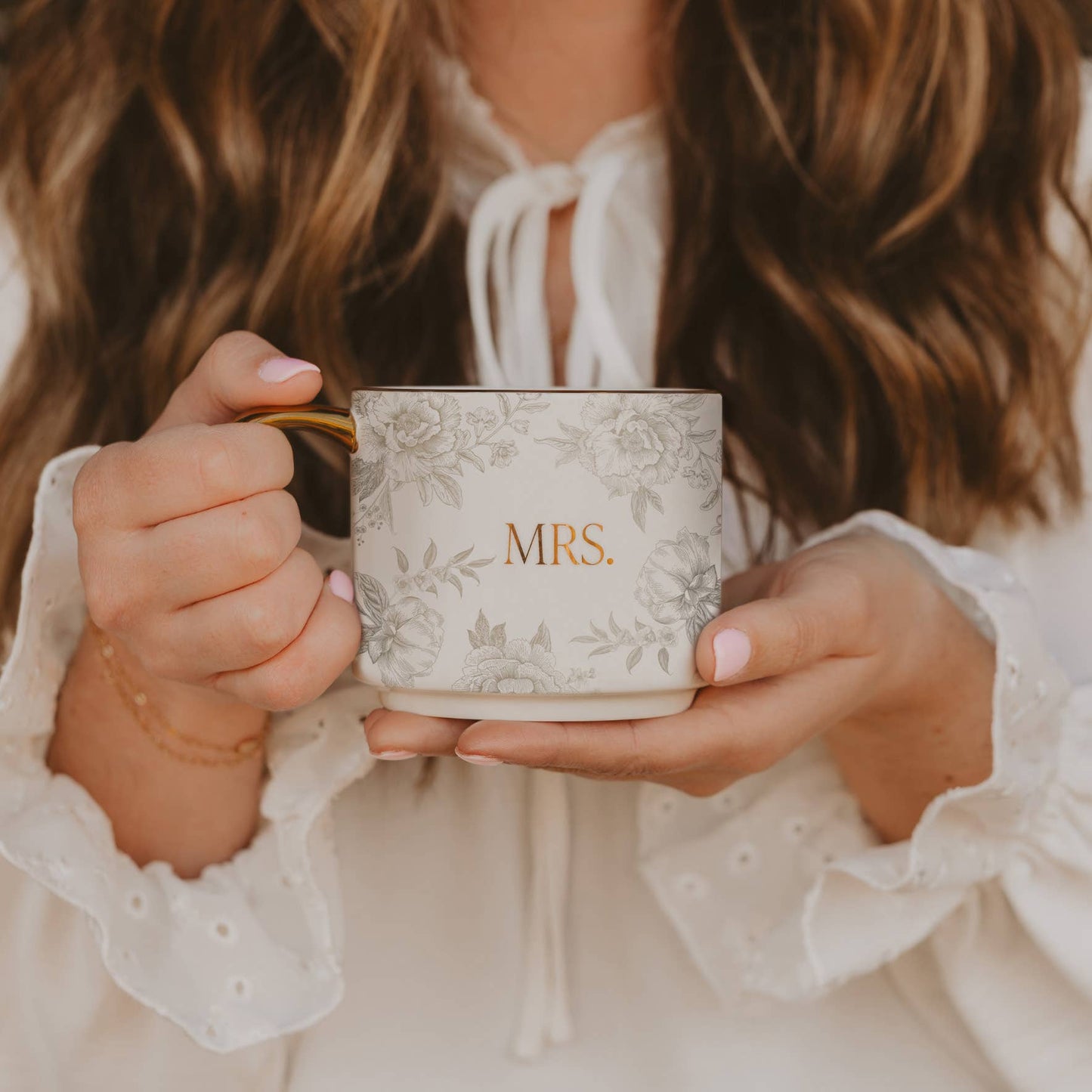 Person holding a mug with 'MRS' on it, wearing a white blouse.