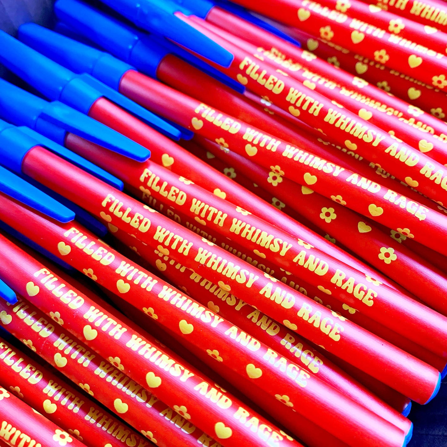 Red pens with blue accents and text 'Filled with Whimsy and Rage' on a dark background