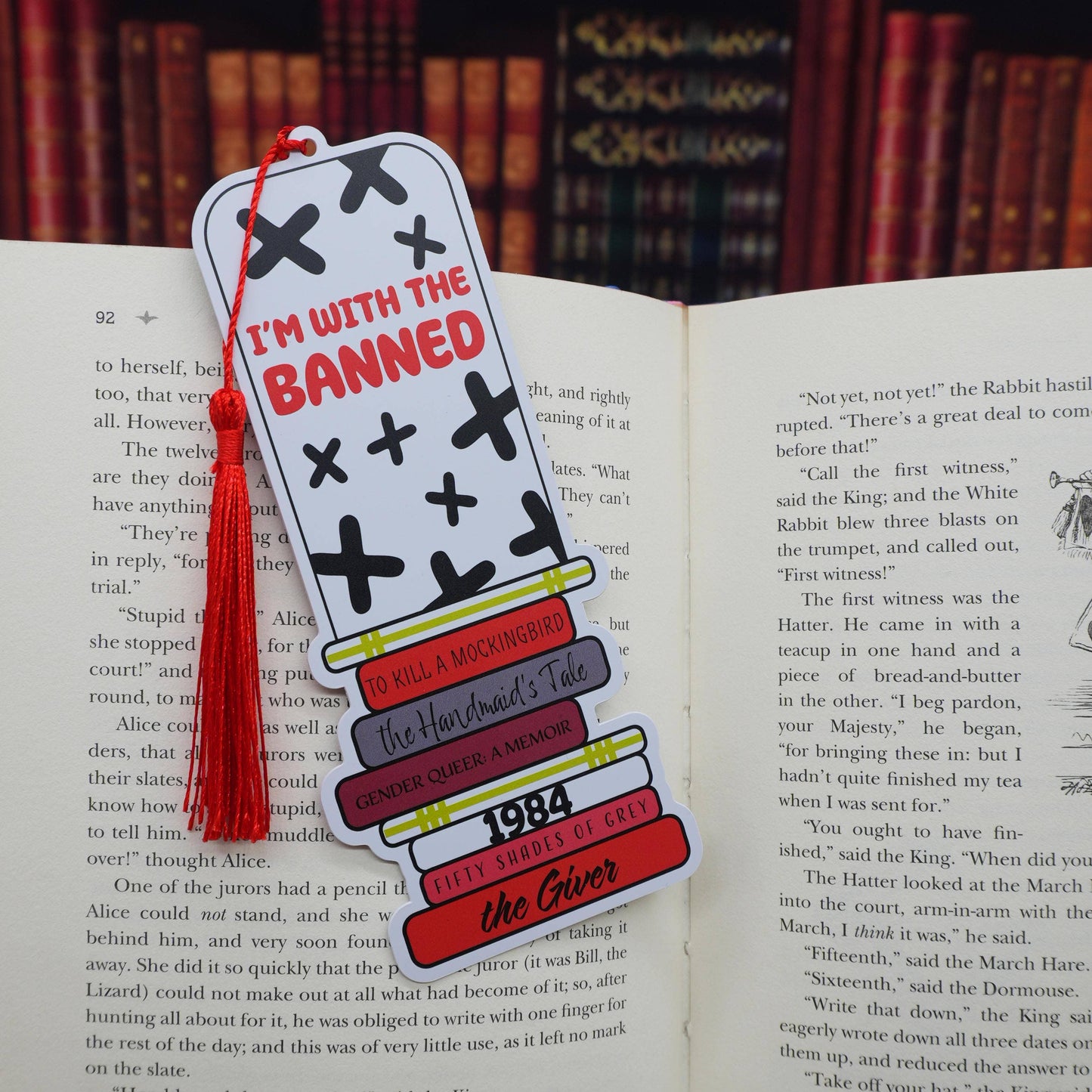 Bookmark of a stack of banned books and 'I'm with the Banned' text, and a red tassle on an open book