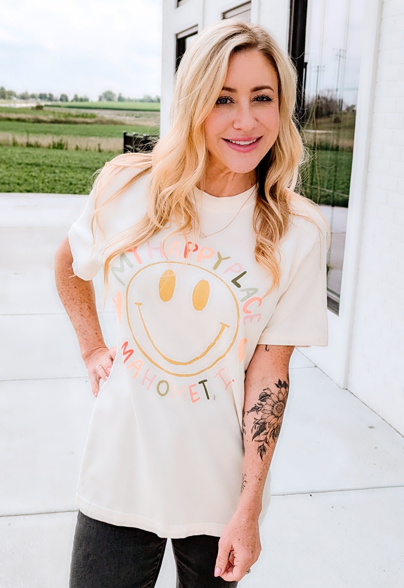 A woman smiling and wearing a white t-shirt with the text 'MY HAPPY PLACE MAHOMET' printed around a smiley face on the front.
