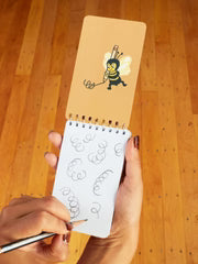 Person holding a small notebook with a bee illustration on a wooden surface