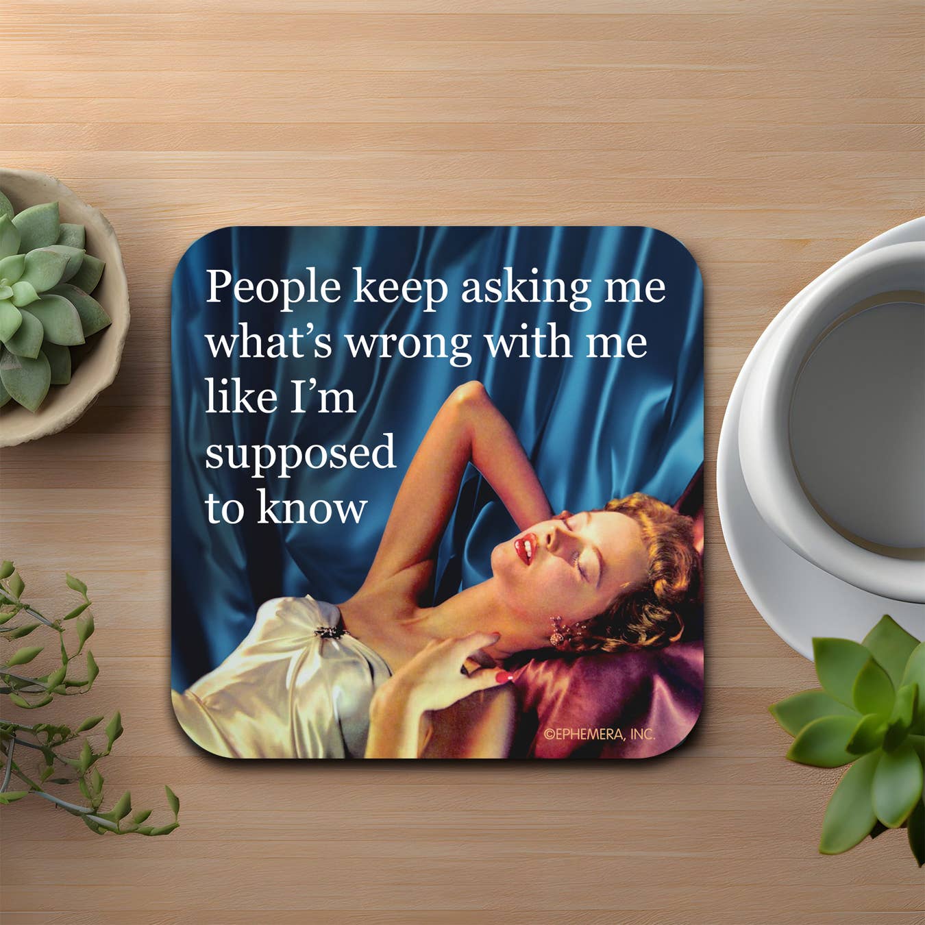 Coaster with a quote on a wooden surface with a cup and plants