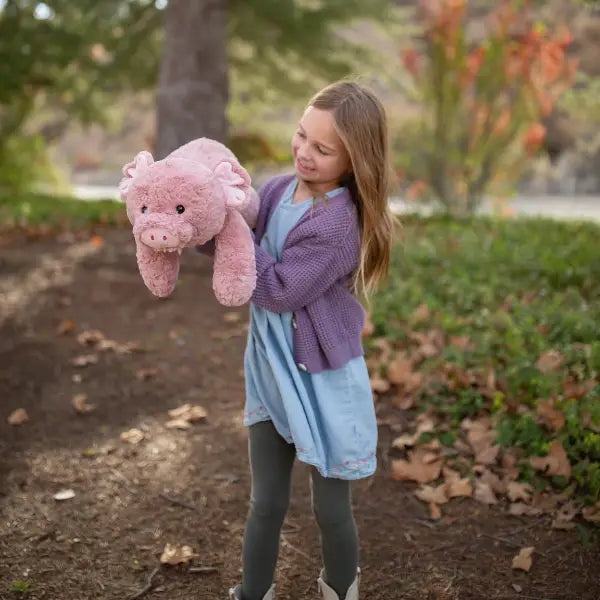 Girl holding a pink stuffed pig in a park setting