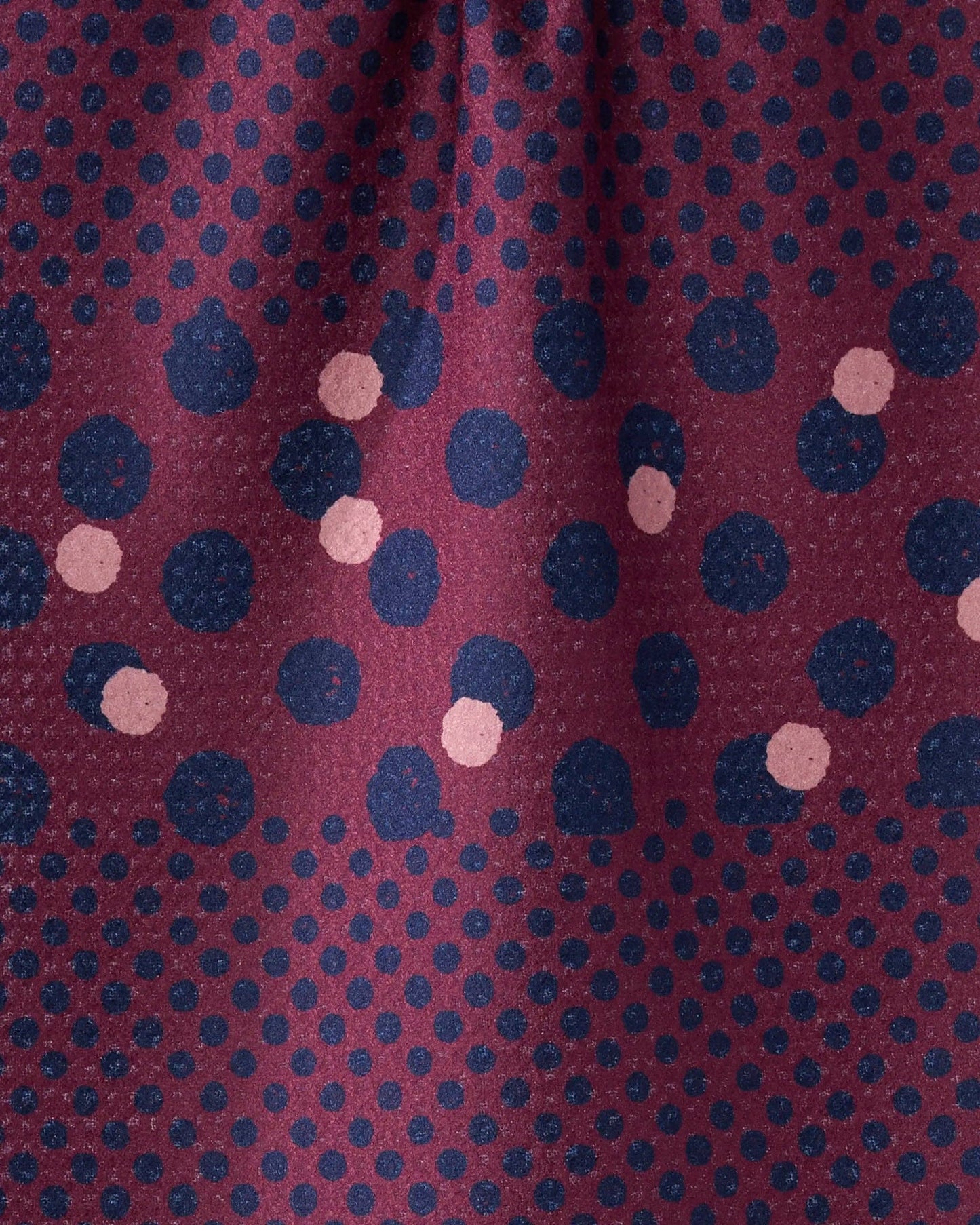 A close-up of a patterned fabric with a deep burgundy base, covered in small navy blue dots and larger scattered navy and dusty pink polka dots.