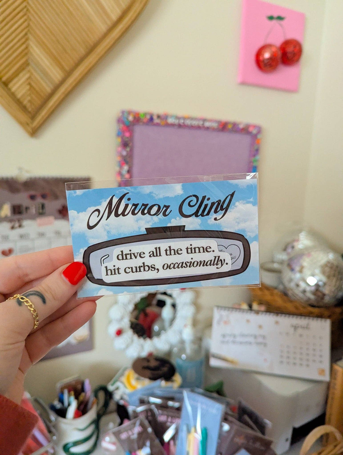 Hand holding a 'Mirror Cling' product with humorous text in a casual indoor setting.