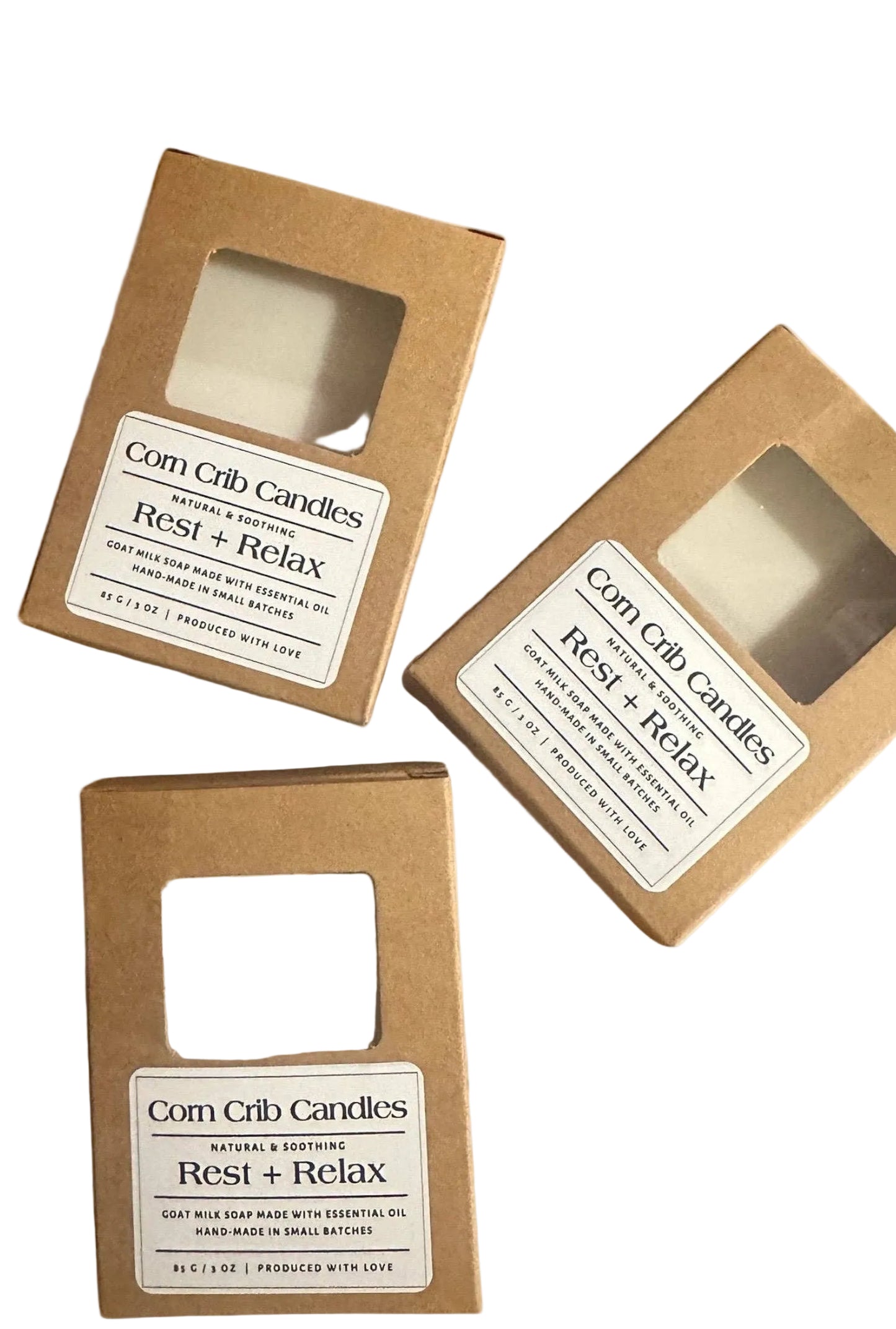 Three boxes of Corn Crib Candles labeled 'Rest + Relax' on a marble surface with lavender flowers.