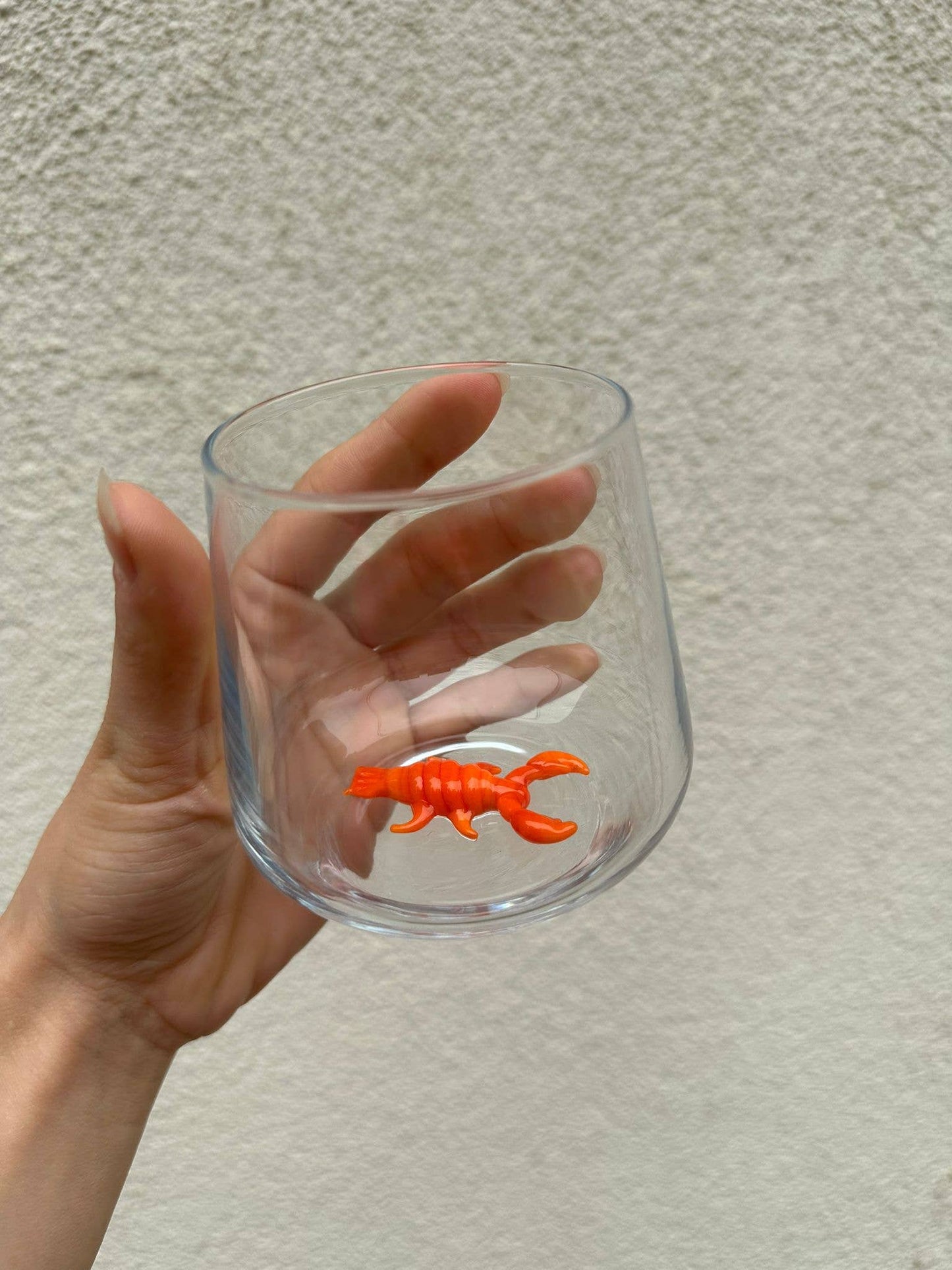 Clear glass with an orange lobster charm held by a hand against a neutral background