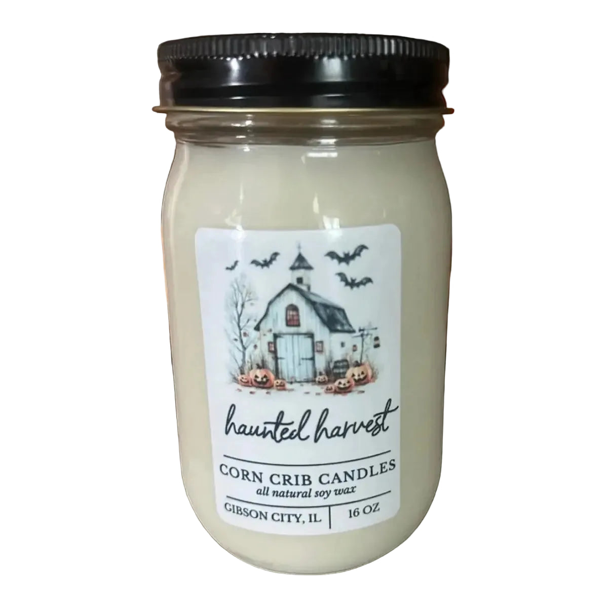 A 16 oz mason jar candle with a black lid and a white label reading 'haunted harvest Corn Crib Candles' with a haunted house illustration, set on a rustic wooden surface with pumpkins in the background.