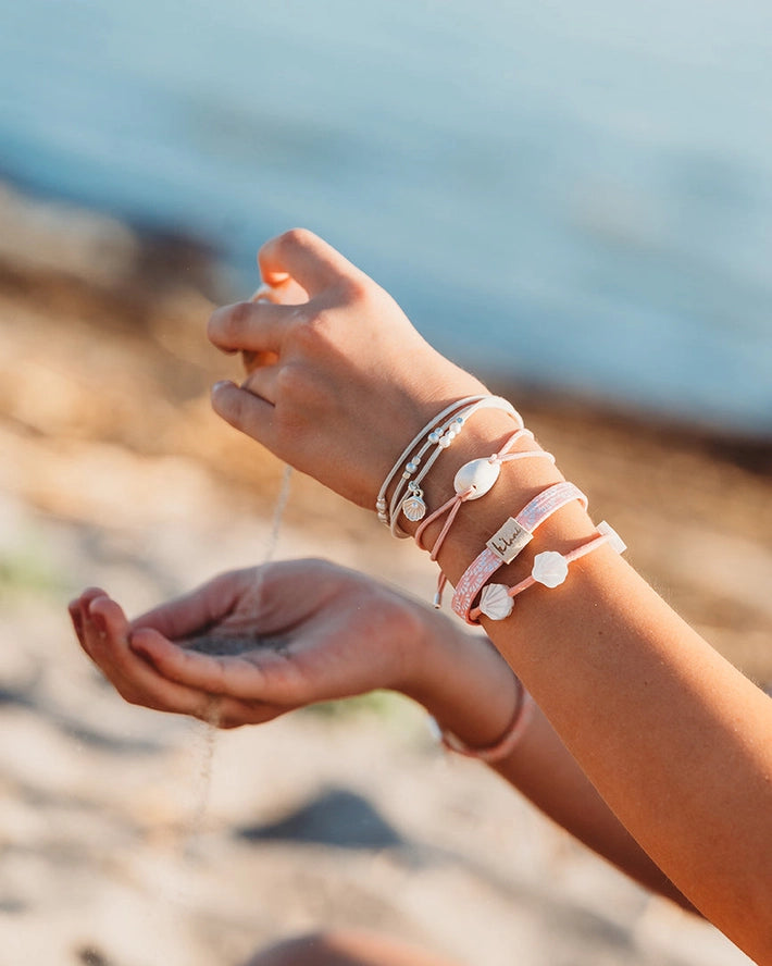 Person wearing multiple bracelets on a beach with water in the background