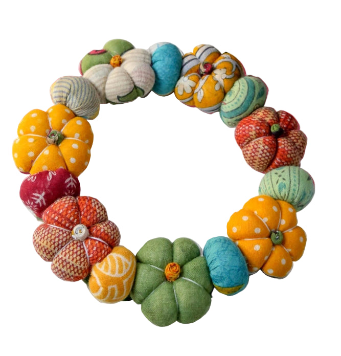 Colorful fabric pumpkins arranged in a circular wreath on a white background