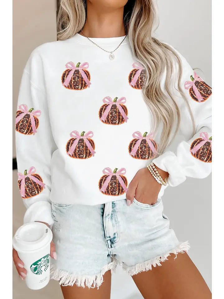 Person wearing a white sweatshirt with pumpkin sequin patches and denim shorts, holding a Starbucks cup.