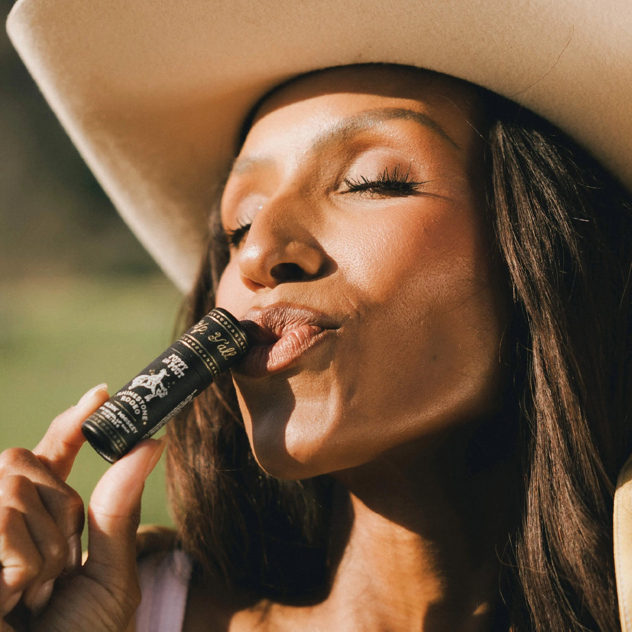 Woman wearing a beige hat and holding a black lip balm.