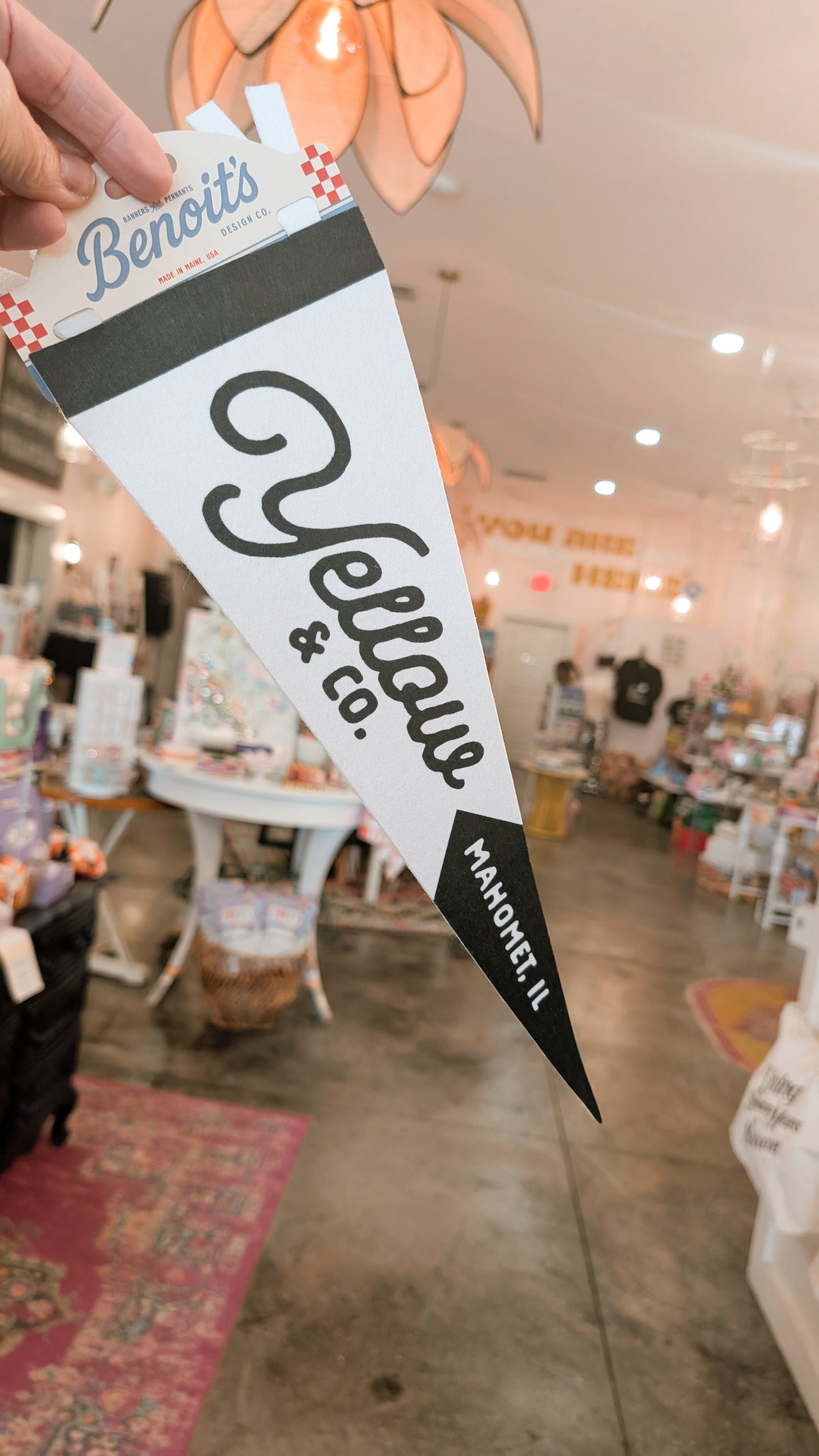 Hand holding a 'Benoit's Yellow Co.' branded flag inside a store.