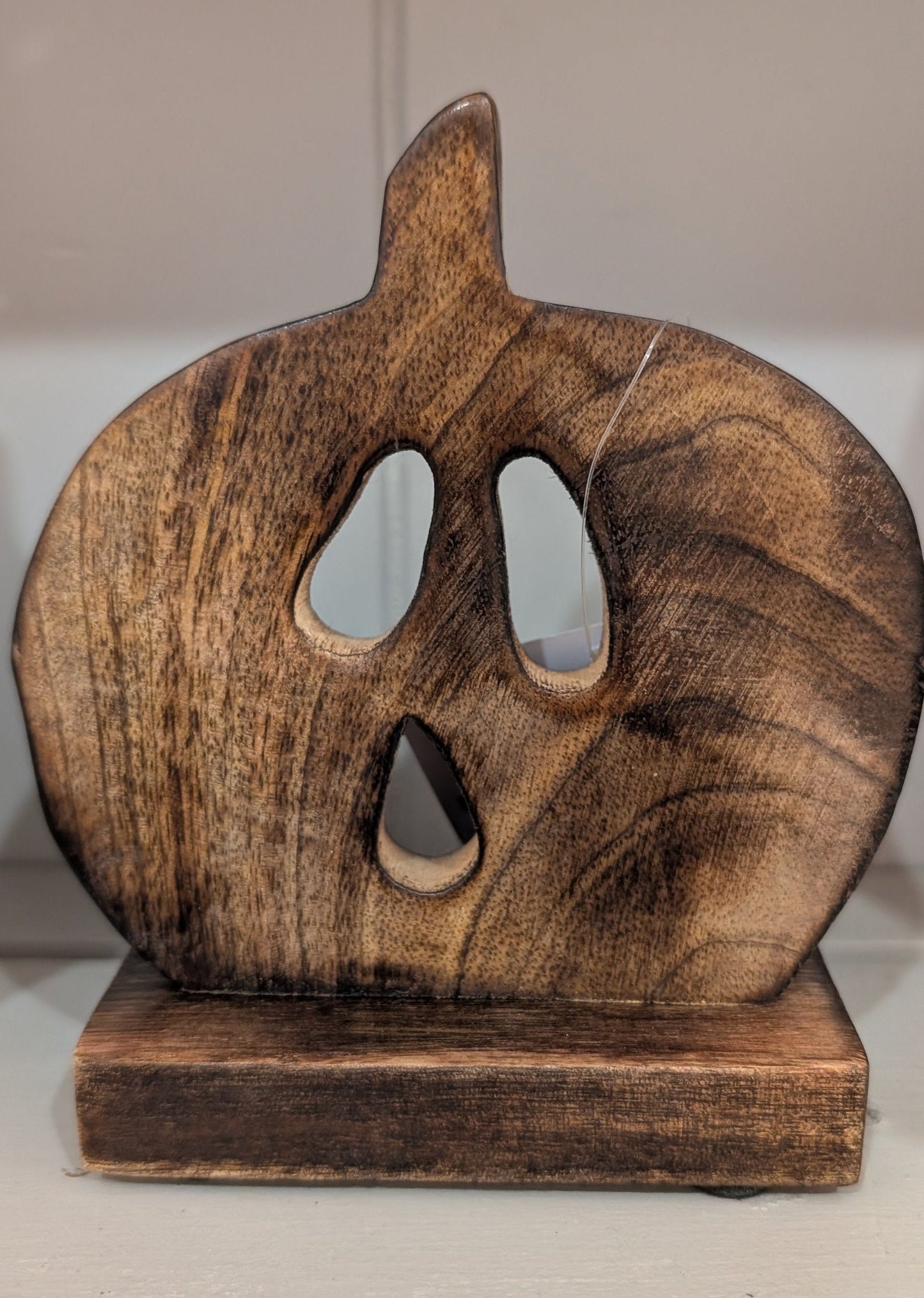 A rustic, handcrafted wooden jack-o'-lantern decoration with carved eyes and mouth, resting on a matching wooden base against a plain indoor background.