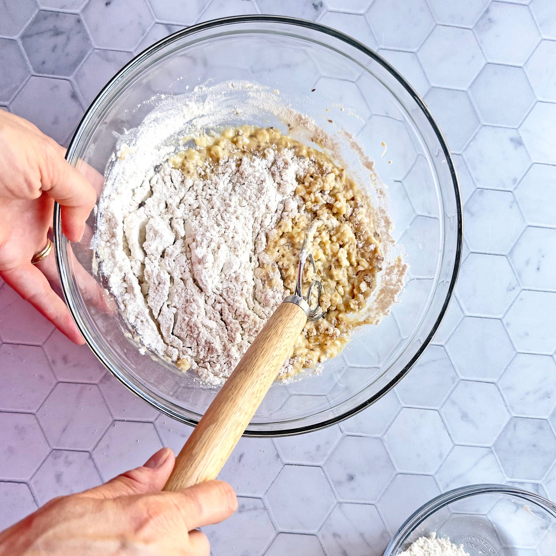 Person mixing ingredients in a glass bowl on a tiled countertop