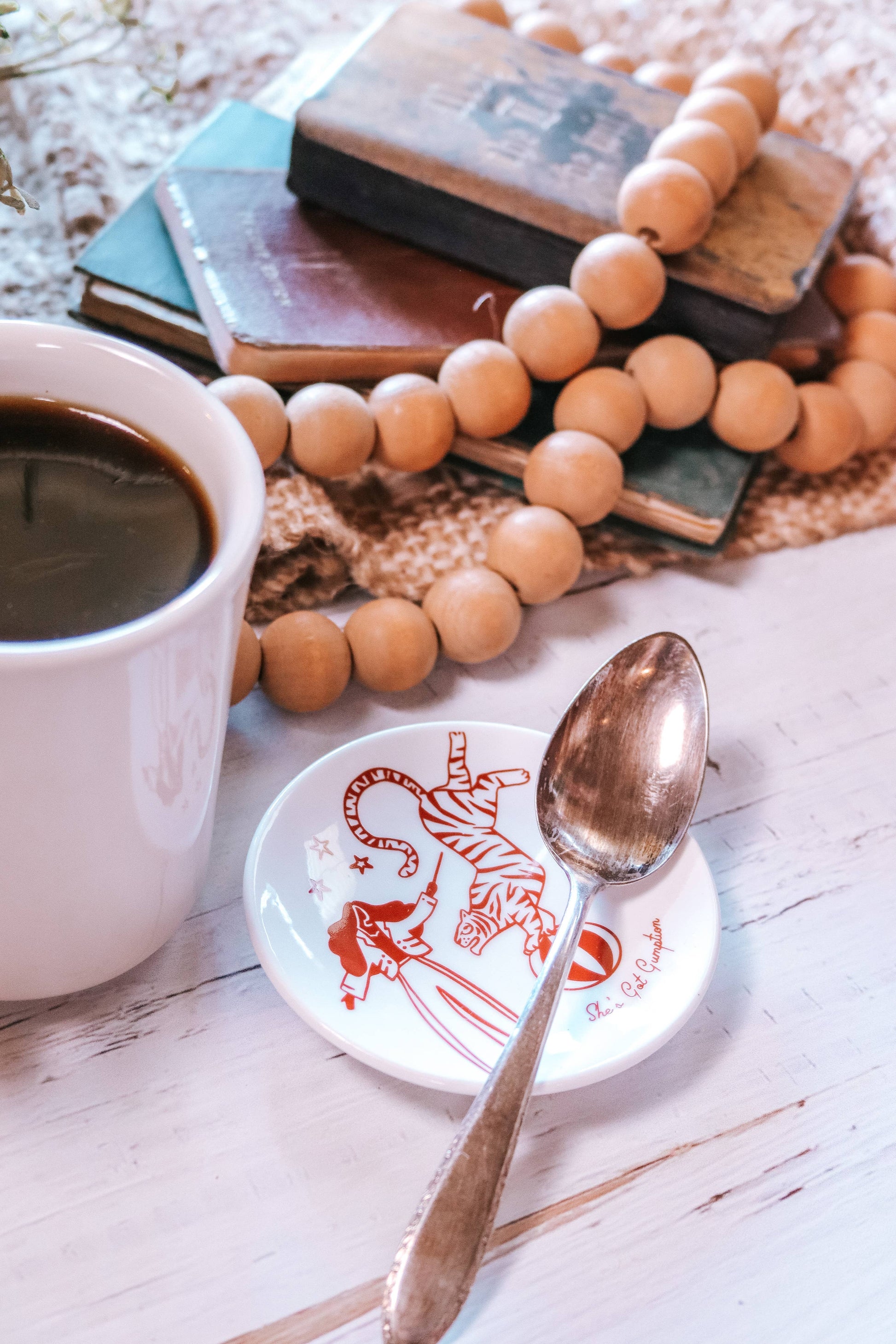 Cup of coffee with a spoon on a coaster, books, and wooden beads on a textured surface