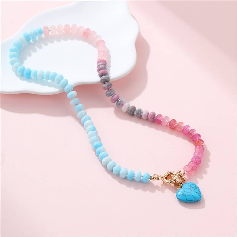 Colorful beaded necklace with a turquoise heart charm on a light pink background