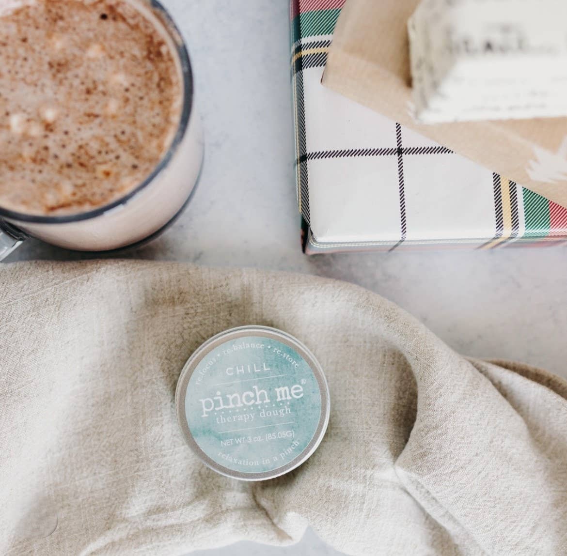 Pinch me therapy dough sitting next to a cup of coffee and a box