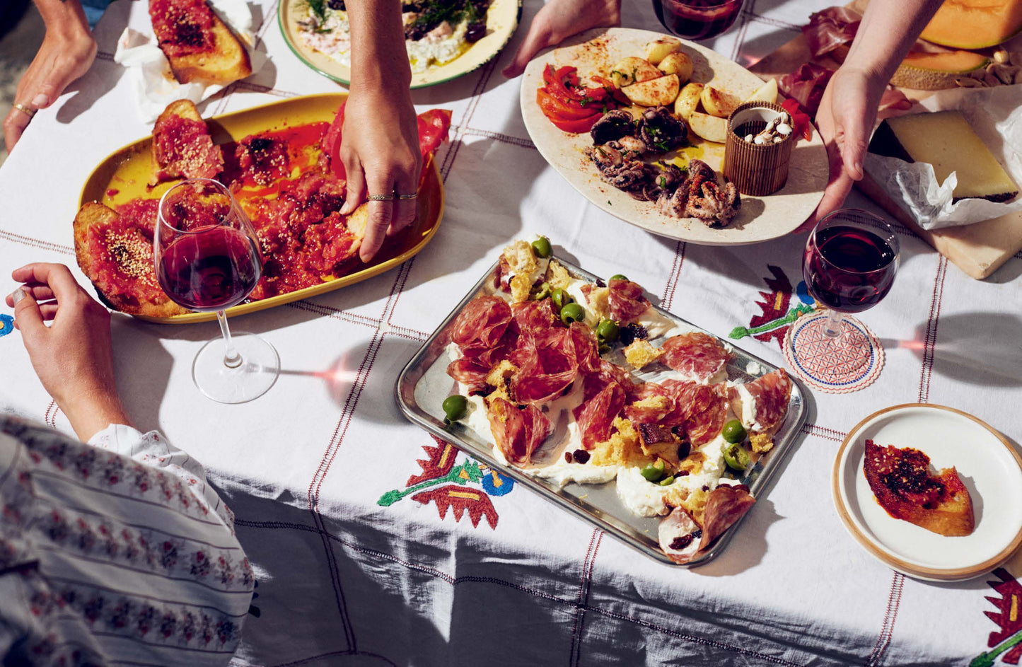 People enjoying a meal with various dishes including pizza and wine on a table.