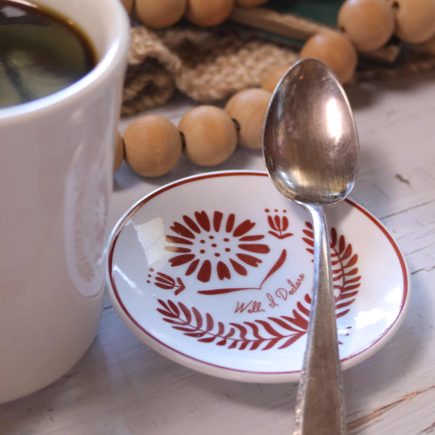 White mug with a floral design, a spoon, and a decorative plate on a wooden surface.