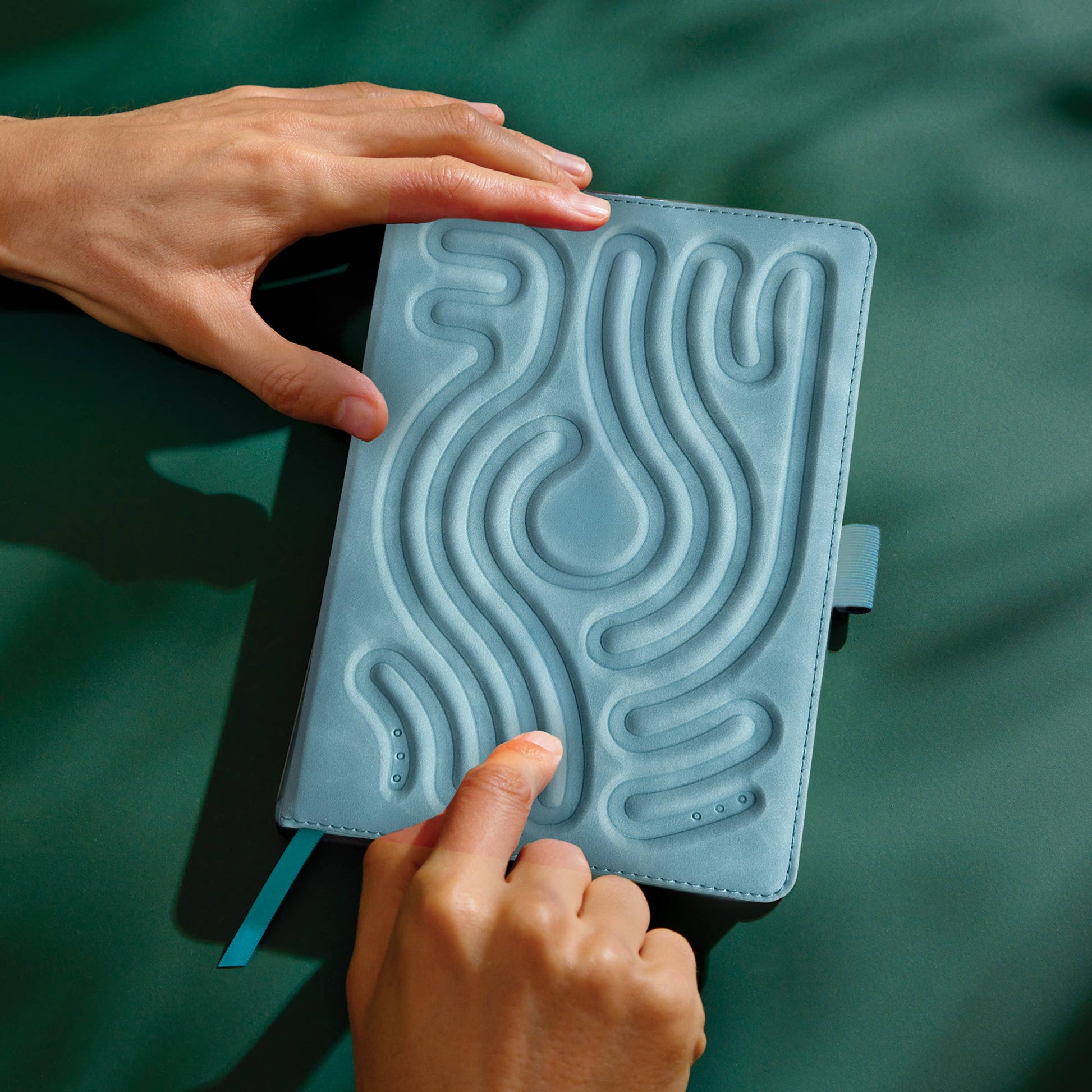 Finger tracing finger maze indent on cover of blue notebook, held on a green background