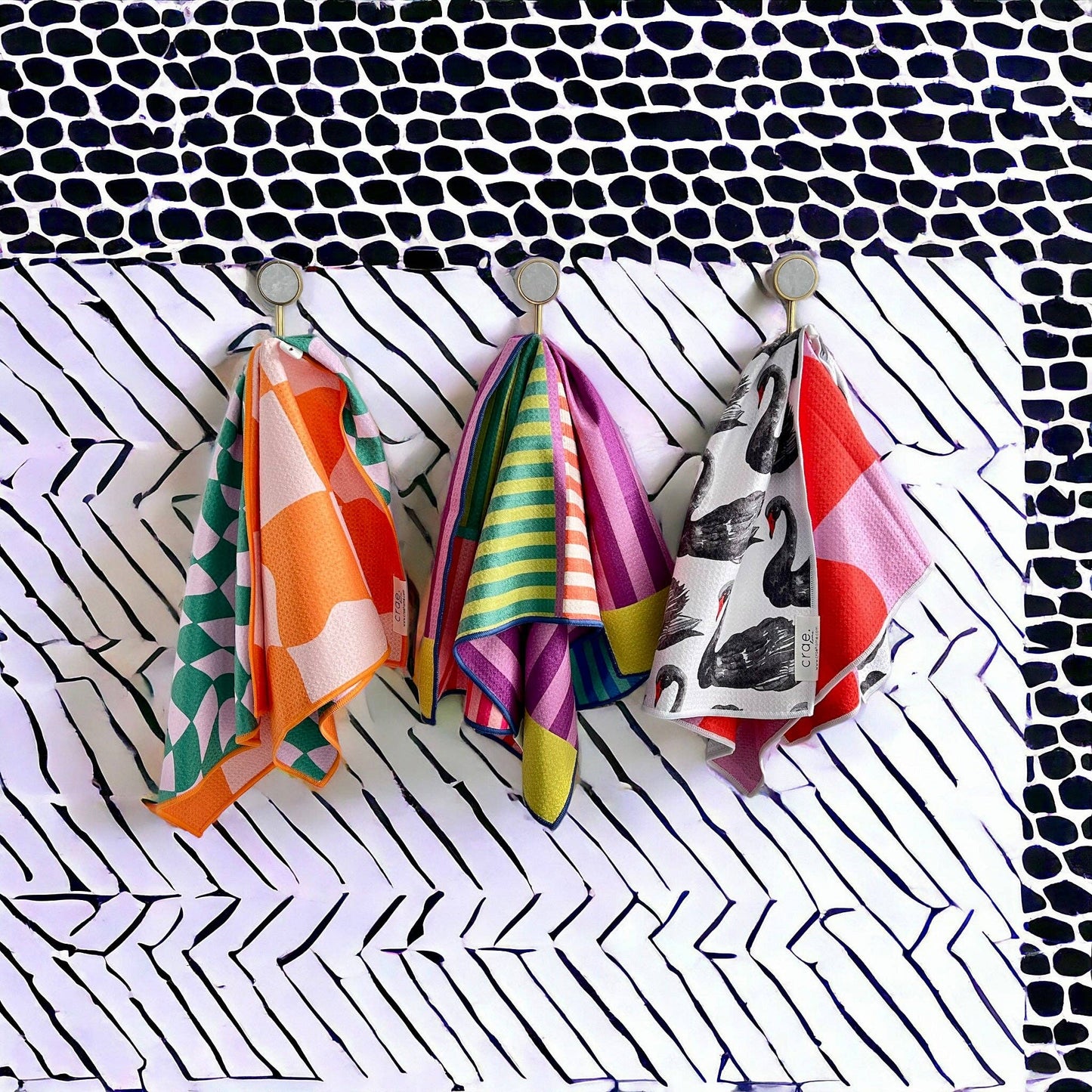 Three colorful hand towels hanging on a hook against a patterned background