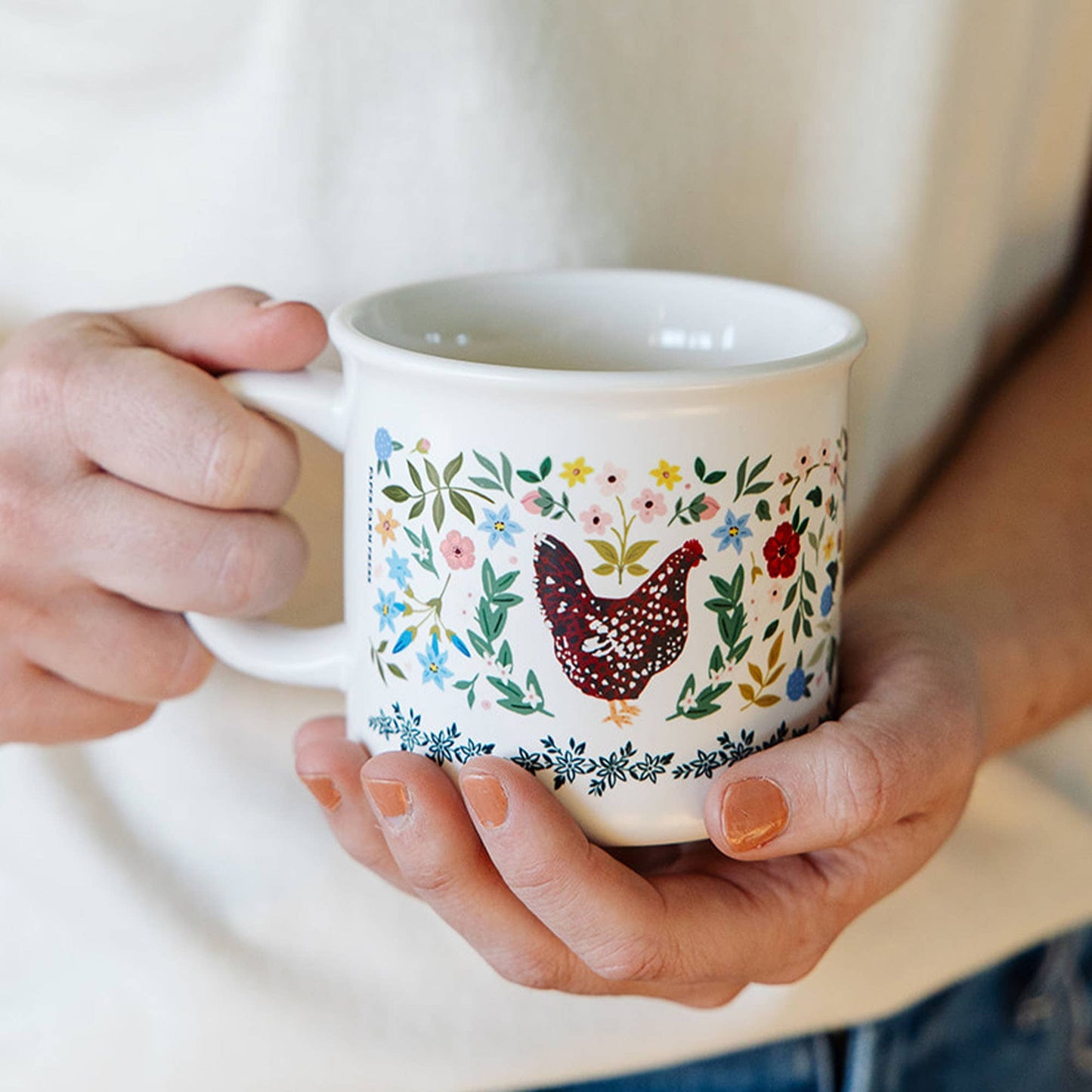 Person holding a mug with a floral and chicken design.
