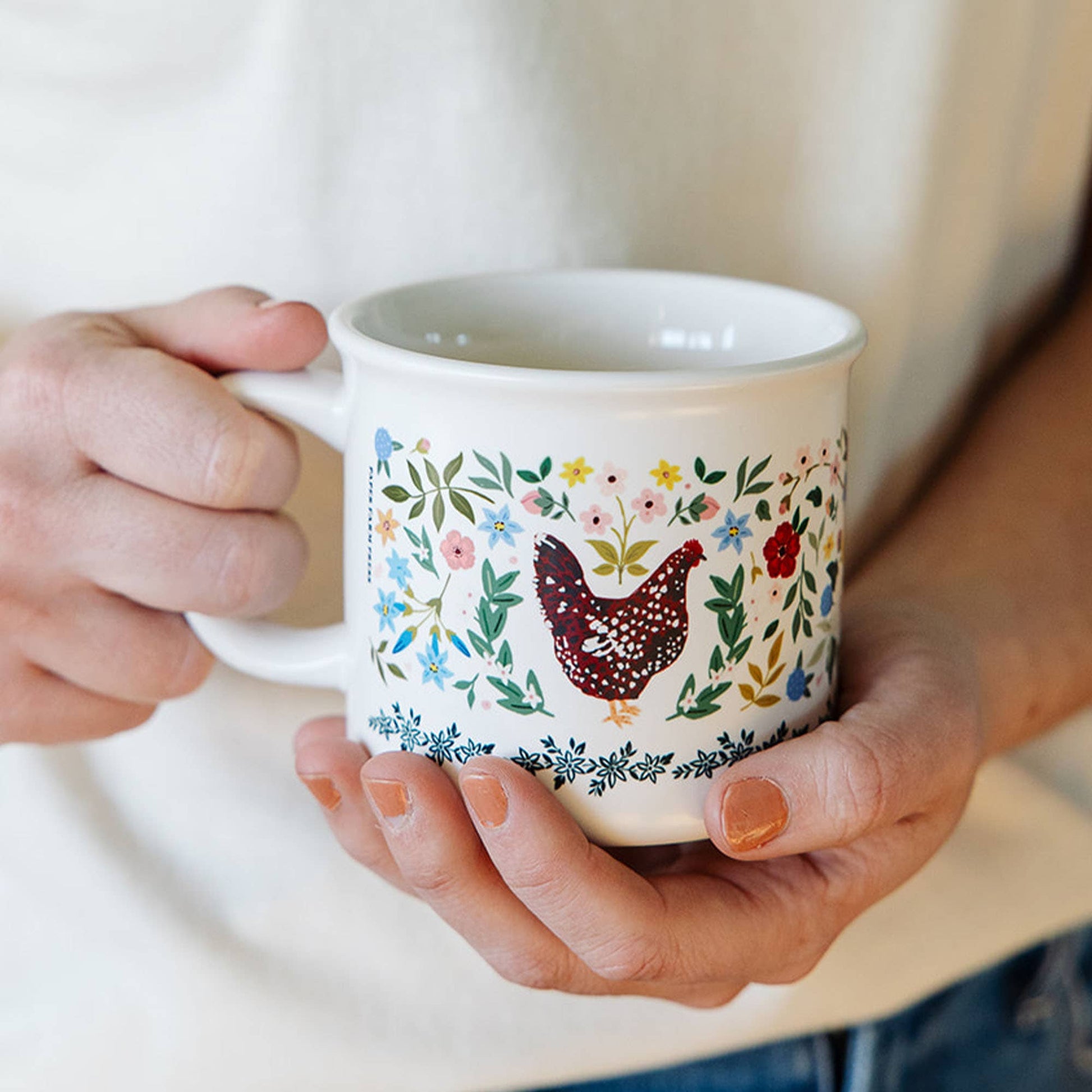 Person holding a mug with a floral and chicken design.
