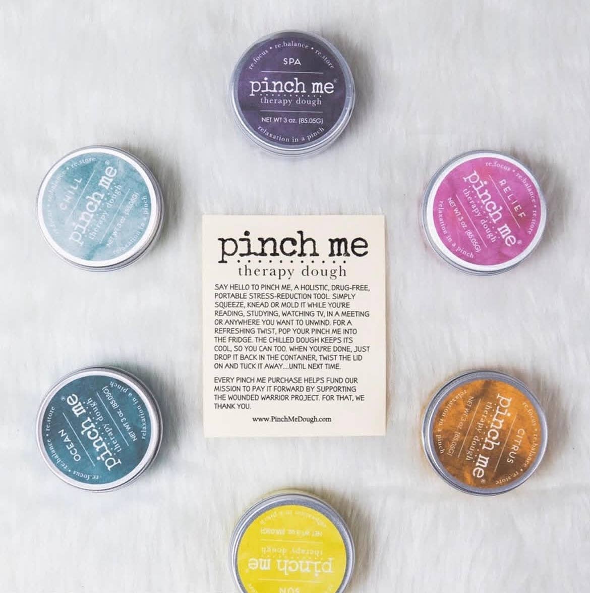 Collection of 'pinch me' therapy dough tins on a textured surface with a card in the center.