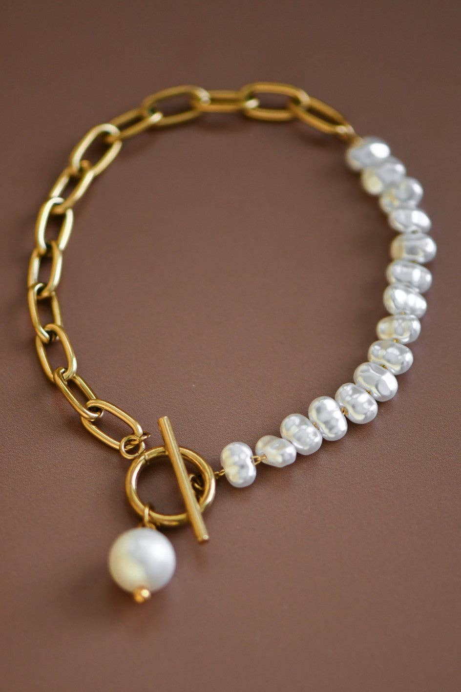 Gold chain bracelet with pearl beads on a brown background