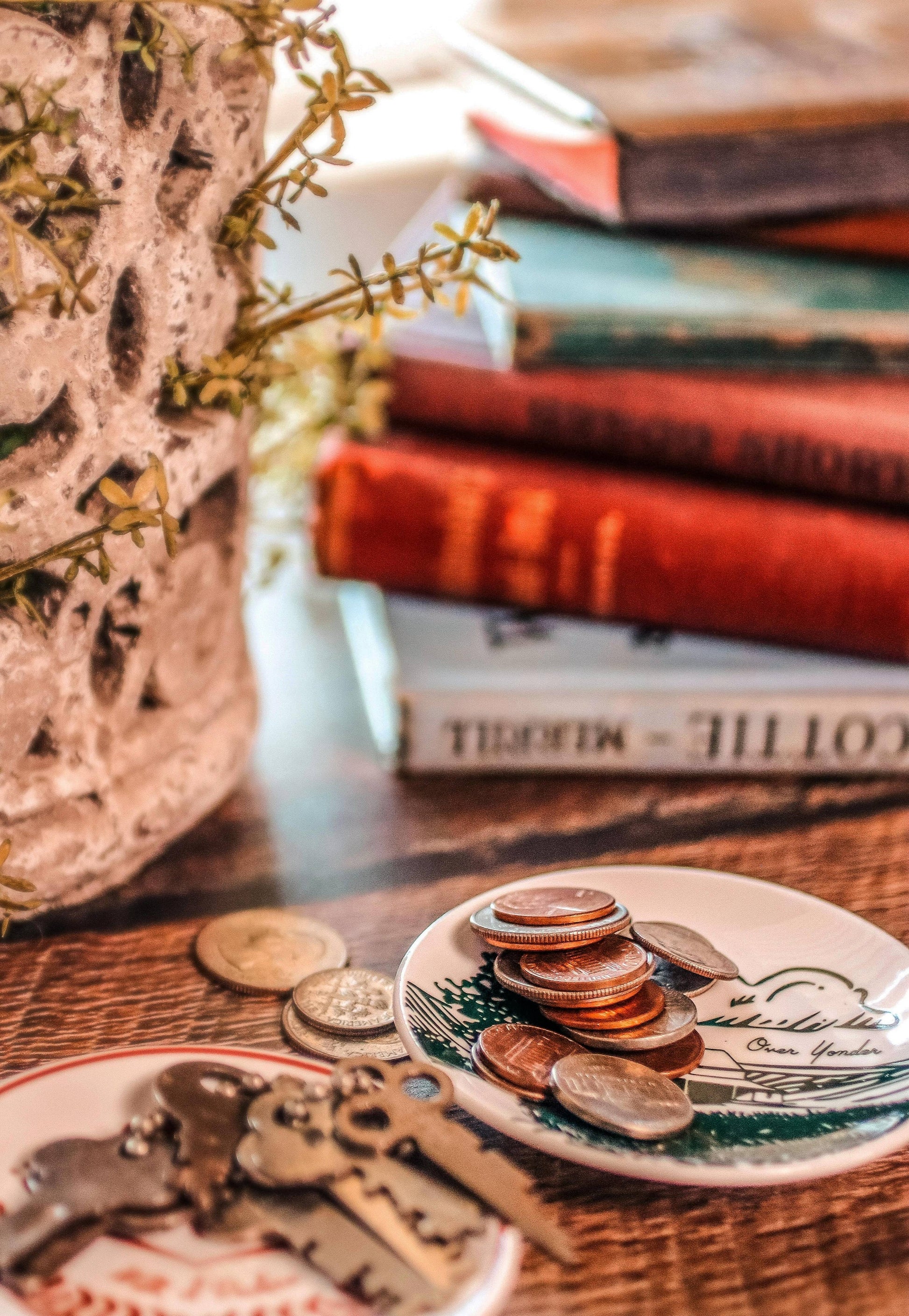 Stack of books with a decorative plate featuring coins on a wooden surface.