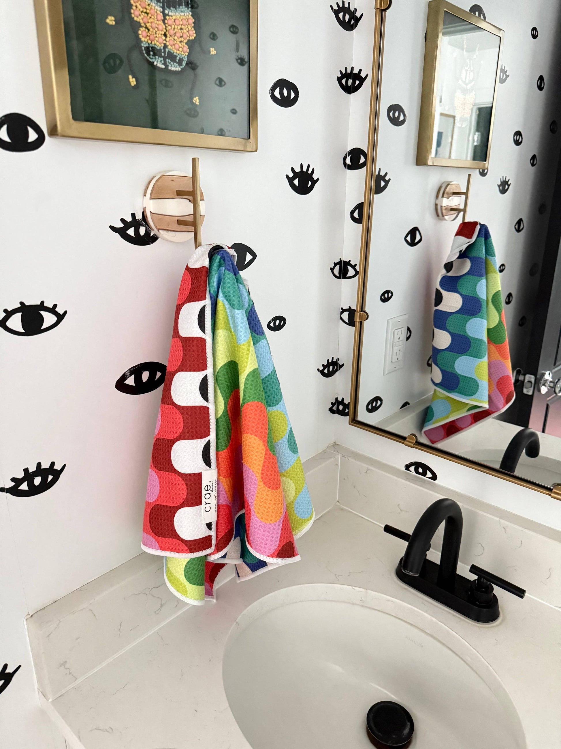 Bathroom with colorful towels hanging on a rack, mirror, and decorative wall patterns.