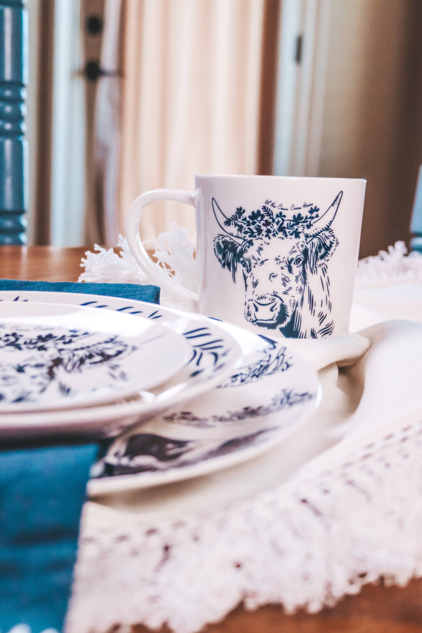 Ceramic mug with a cow design on a table setting with plates and a white napkin.