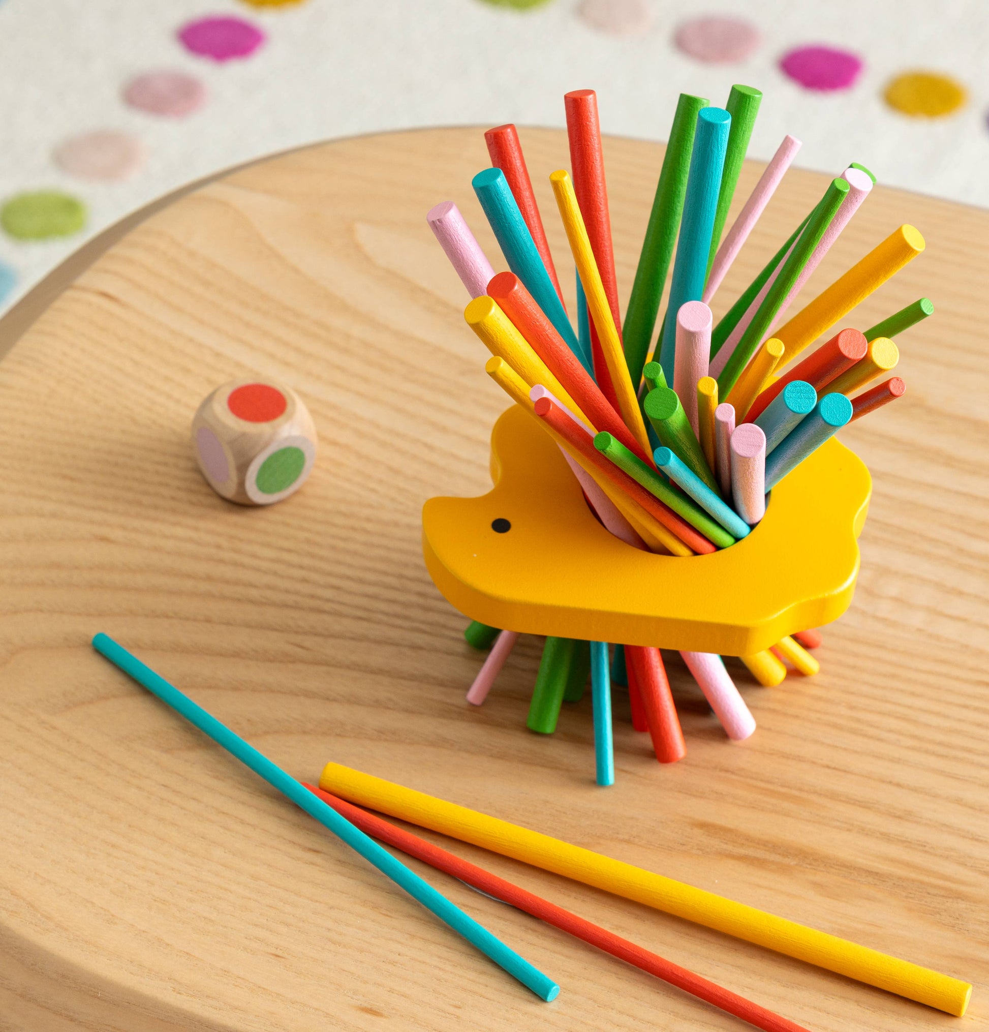 Colorful sticks in a yellow holder on a wooden surface with a dice.